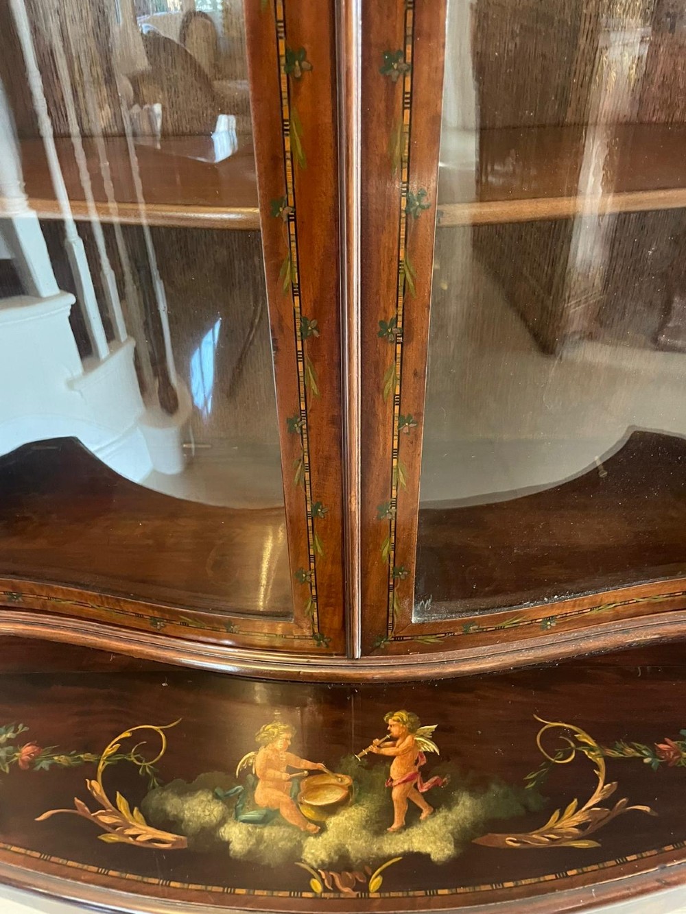 An antique mahogany display cabinet featuring a swan-neck pediment, glazed twin doors, hand-painted floral decoration, and slender tapered legs. View XII