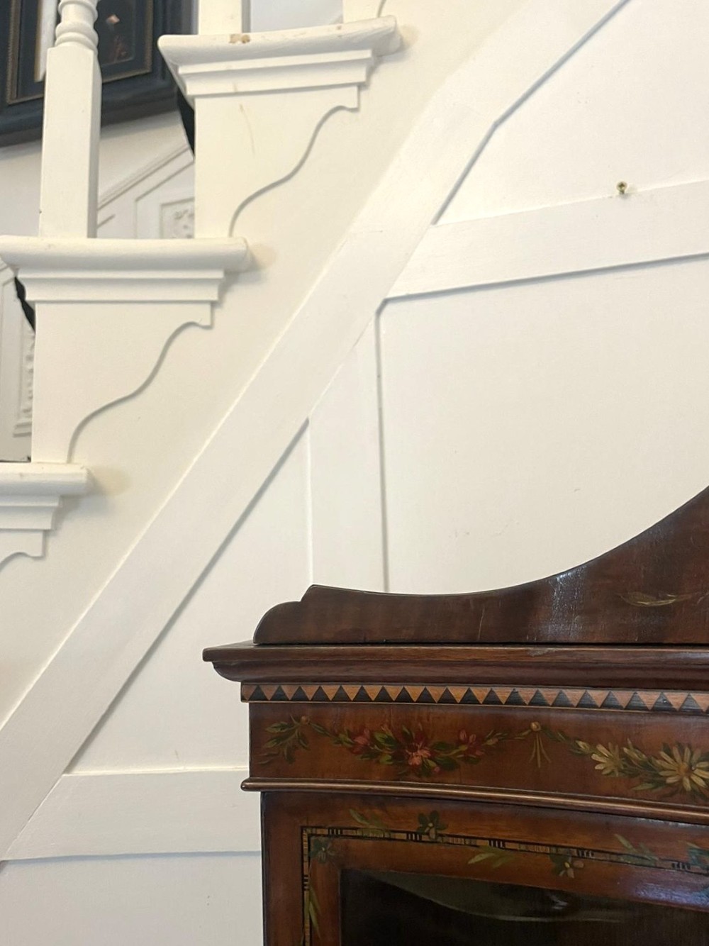 An antique mahogany display cabinet featuring a swan-neck pediment, glazed twin doors, hand-painted floral decoration, and slender tapered legs. View XIII