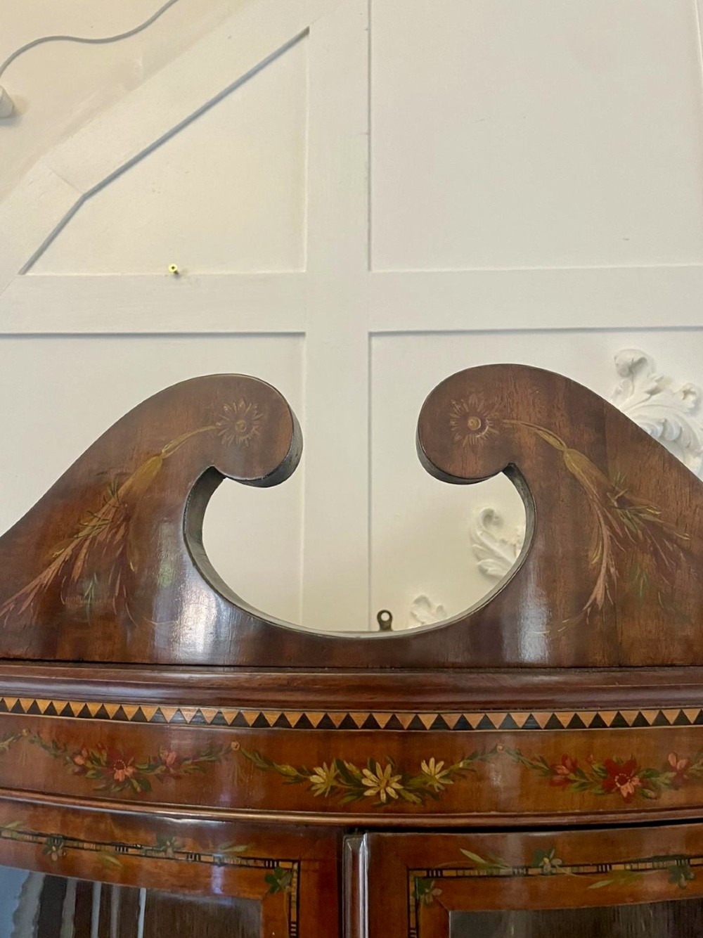 An antique mahogany display cabinet featuring a swan-neck pediment, glazed twin doors, hand-painted floral decoration, and slender tapered legs. View XIV