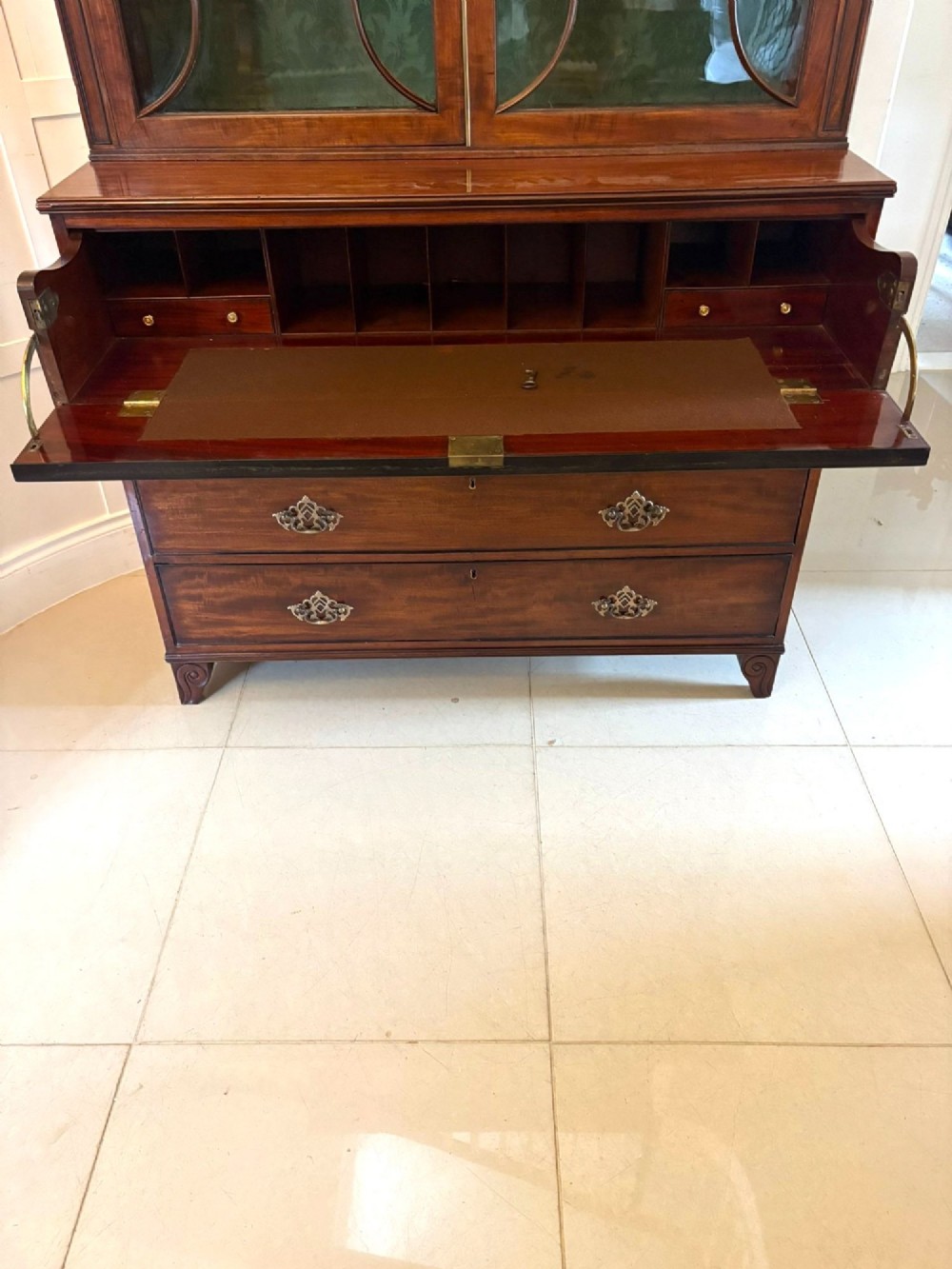 An antique Regency mahogany secretaire bookcase with glazed upper doors featuring curved astragal glazing, resting on a base with four drawers and brass hardware. View V