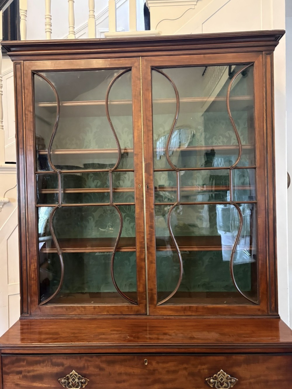 An antique Regency mahogany secretaire bookcase with glazed upper doors featuring curved astragal glazing, resting on a base with four drawers and brass hardware. View VI