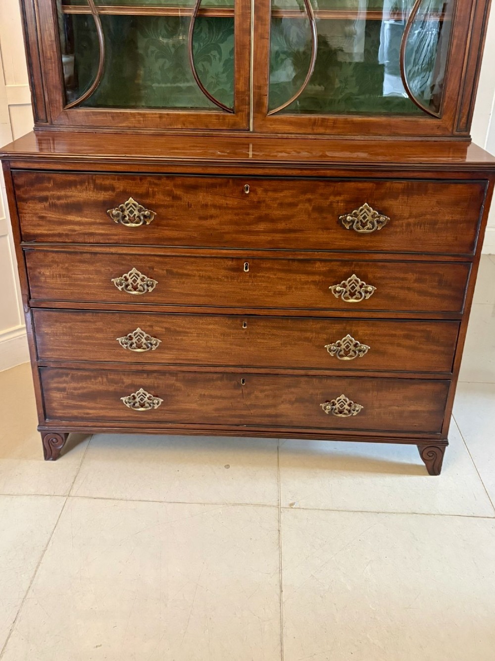 An antique Regency mahogany secretaire bookcase with glazed upper doors featuring curved astragal glazing, resting on a base with four drawers and brass hardware. View X