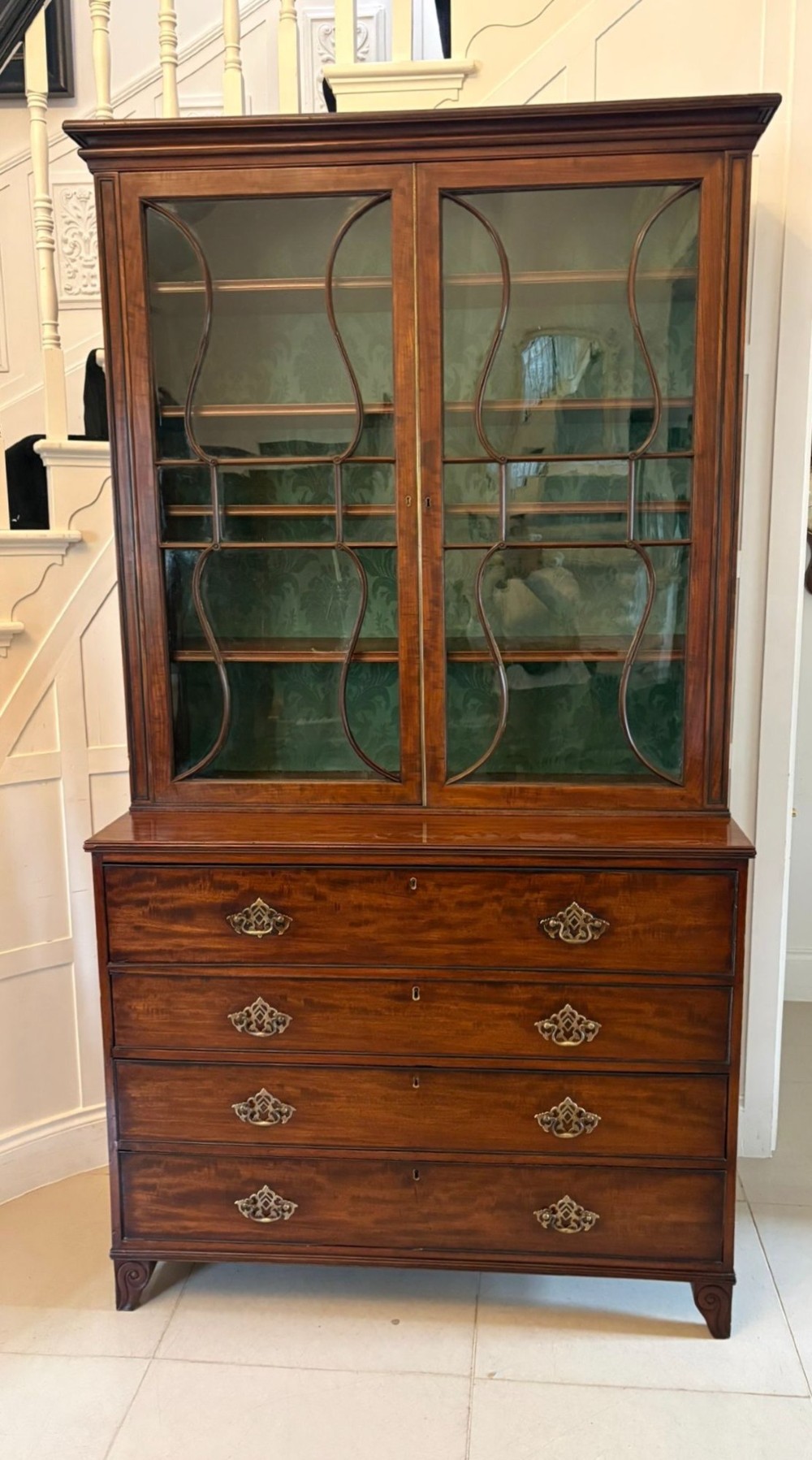 An antique Regency mahogany secretaire bookcase with glazed upper doors featuring curved astragal glazing, resting on a base with four drawers and brass hardware.