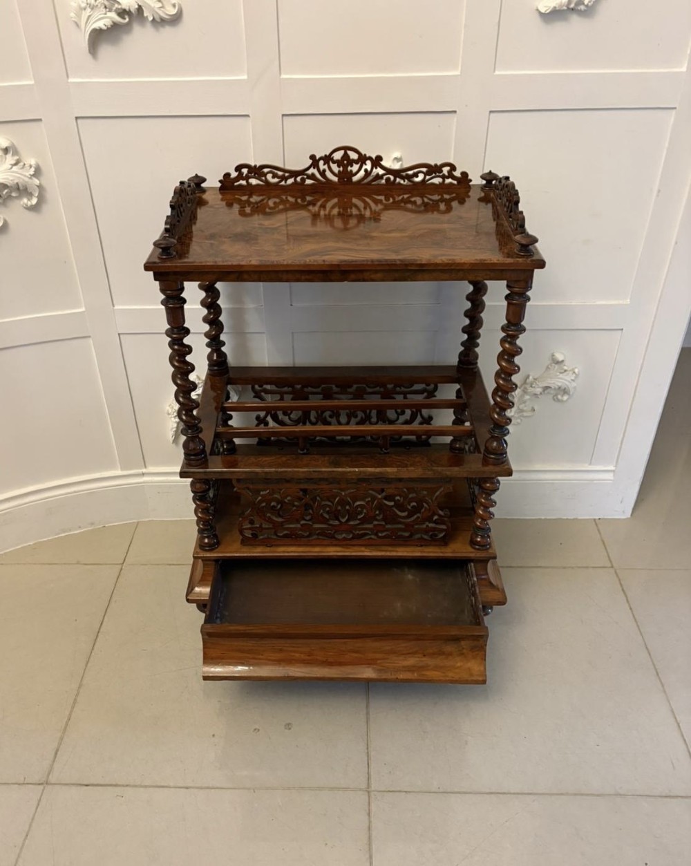 A Victorian burr walnut Canterbury featuring a top surface with a pierced fretwork gallery, barley twist supports, divided slots, and a single drawer resting on porcelain castors. View III