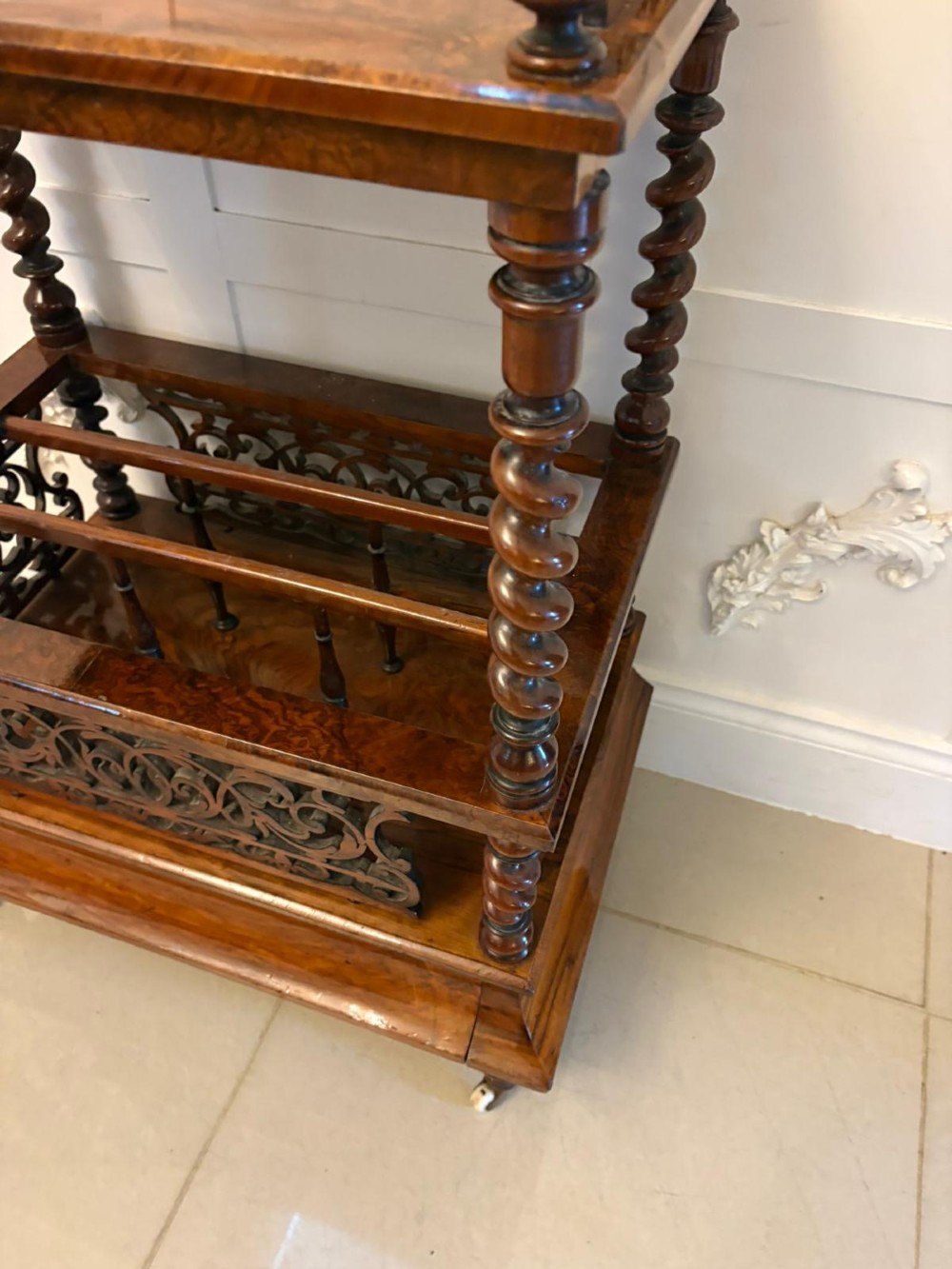 A Victorian burr walnut Canterbury featuring a top surface with a pierced fretwork gallery, barley twist supports, divided slots, and a single drawer resting on porcelain castors. View IV