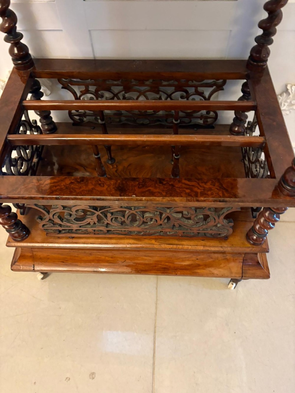 A Victorian burr walnut Canterbury featuring a top surface with a pierced fretwork gallery, barley twist supports, divided slots, and a single drawer resting on porcelain castors. View V