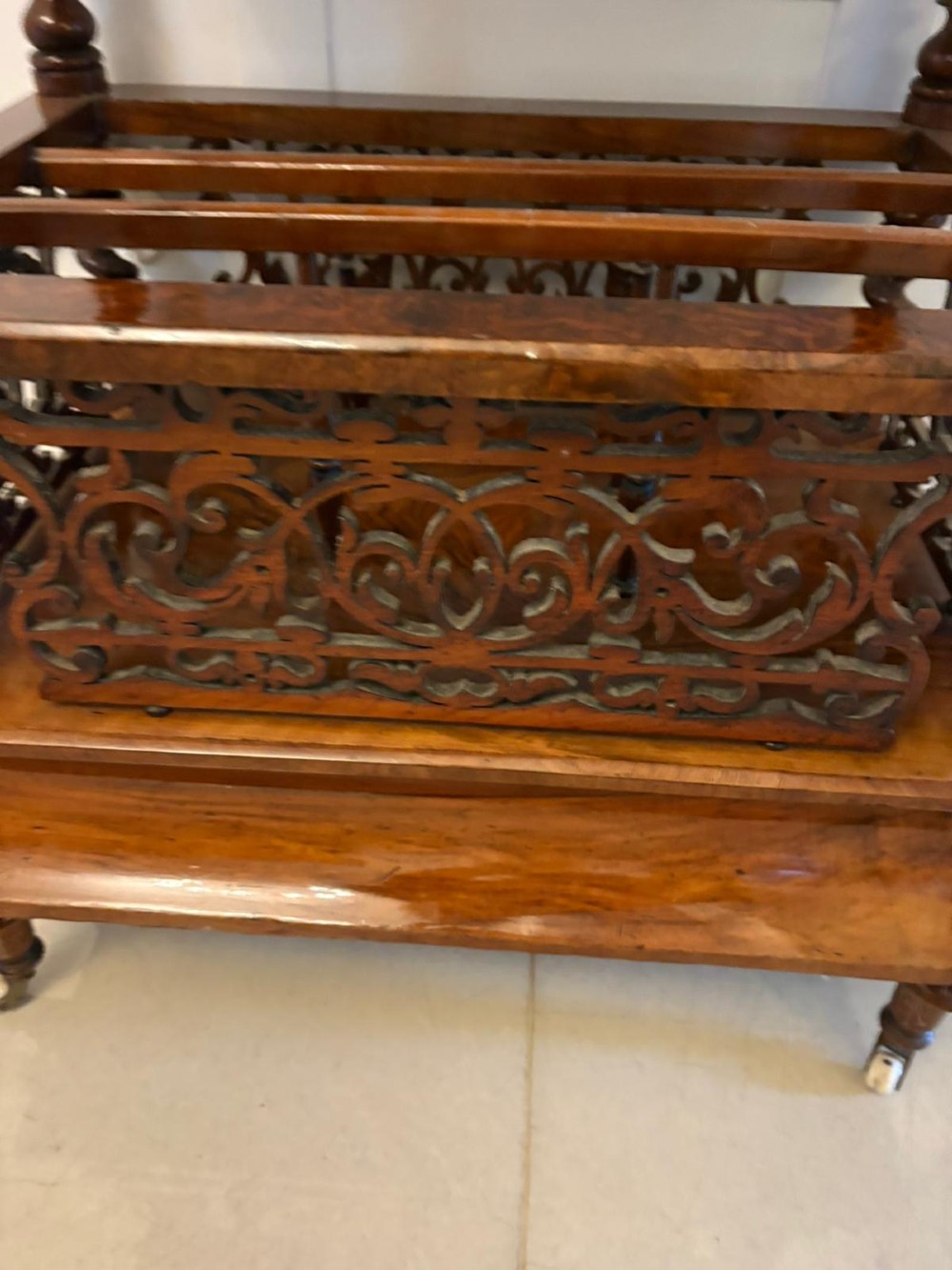 A Victorian burr walnut Canterbury featuring a top surface with a pierced fretwork gallery, barley twist supports, divided slots, and a single drawer resting on porcelain castors. View VI