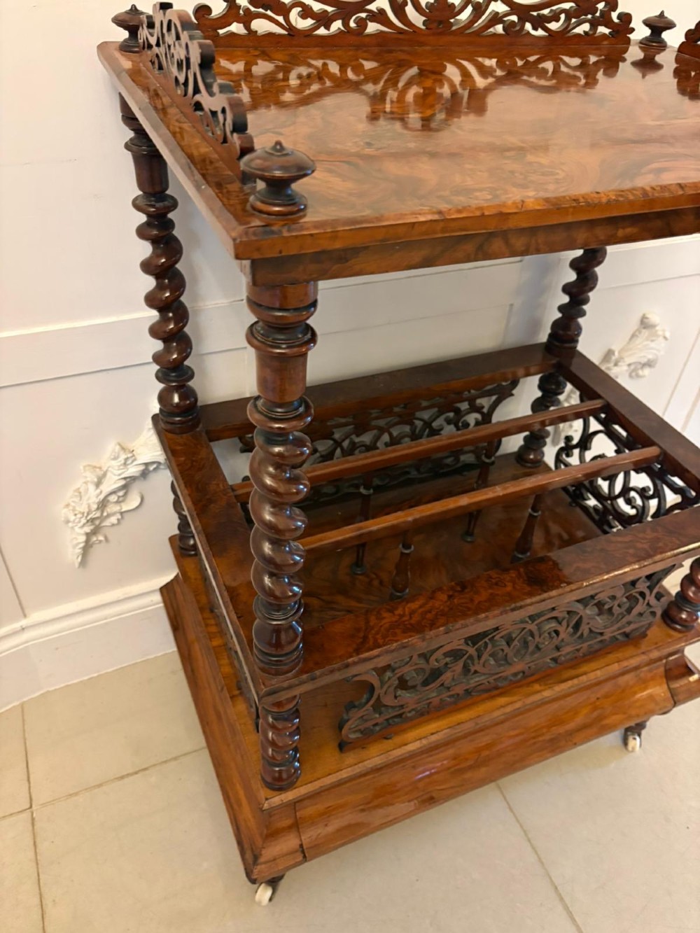 A Victorian burr walnut Canterbury featuring a top surface with a pierced fretwork gallery, barley twist supports, divided slots, and a single drawer resting on porcelain castors. View VII