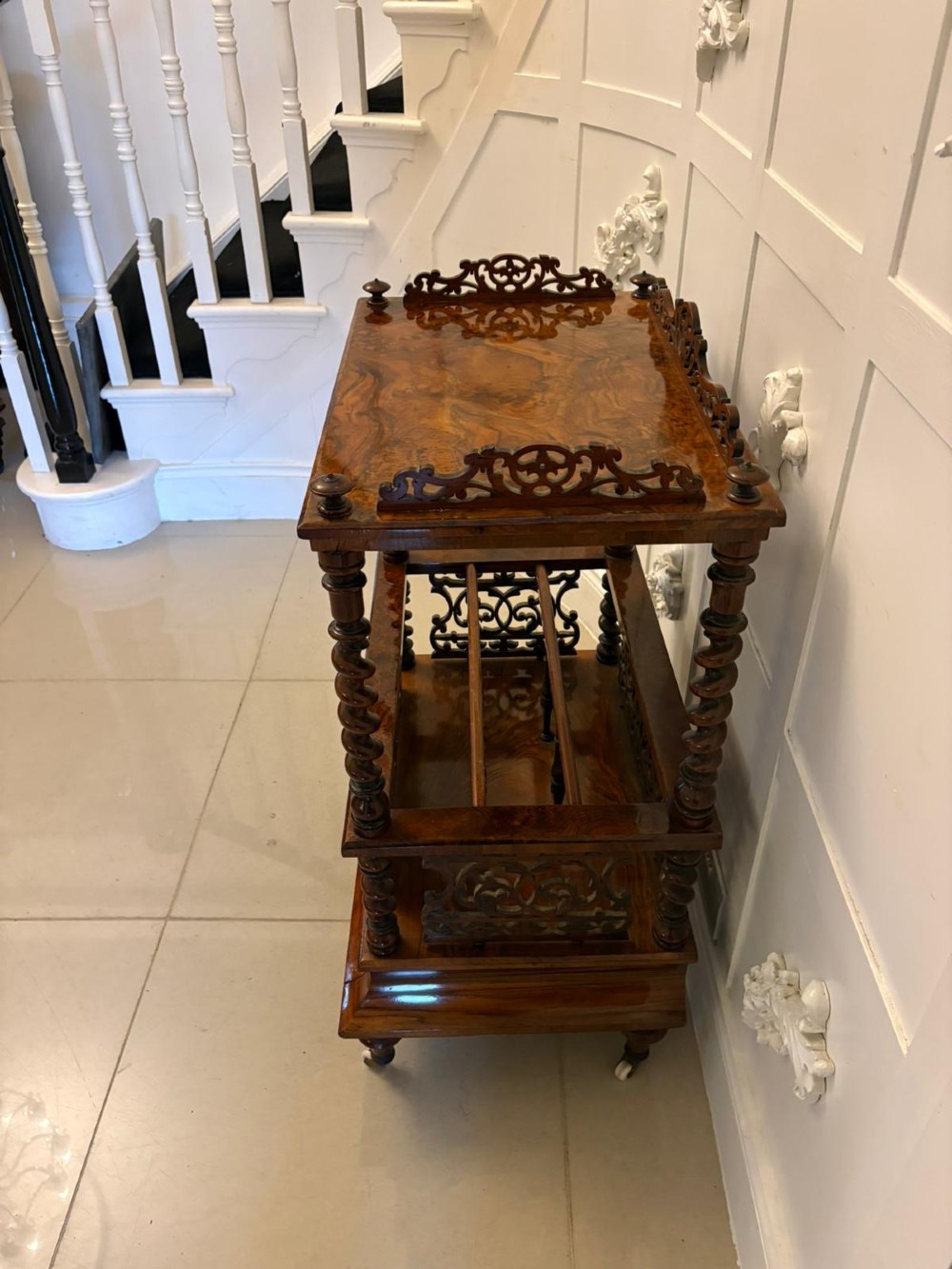 A Victorian burr walnut Canterbury featuring a top surface with a pierced fretwork gallery, barley twist supports, divided slots, and a single drawer resting on porcelain castors. View X