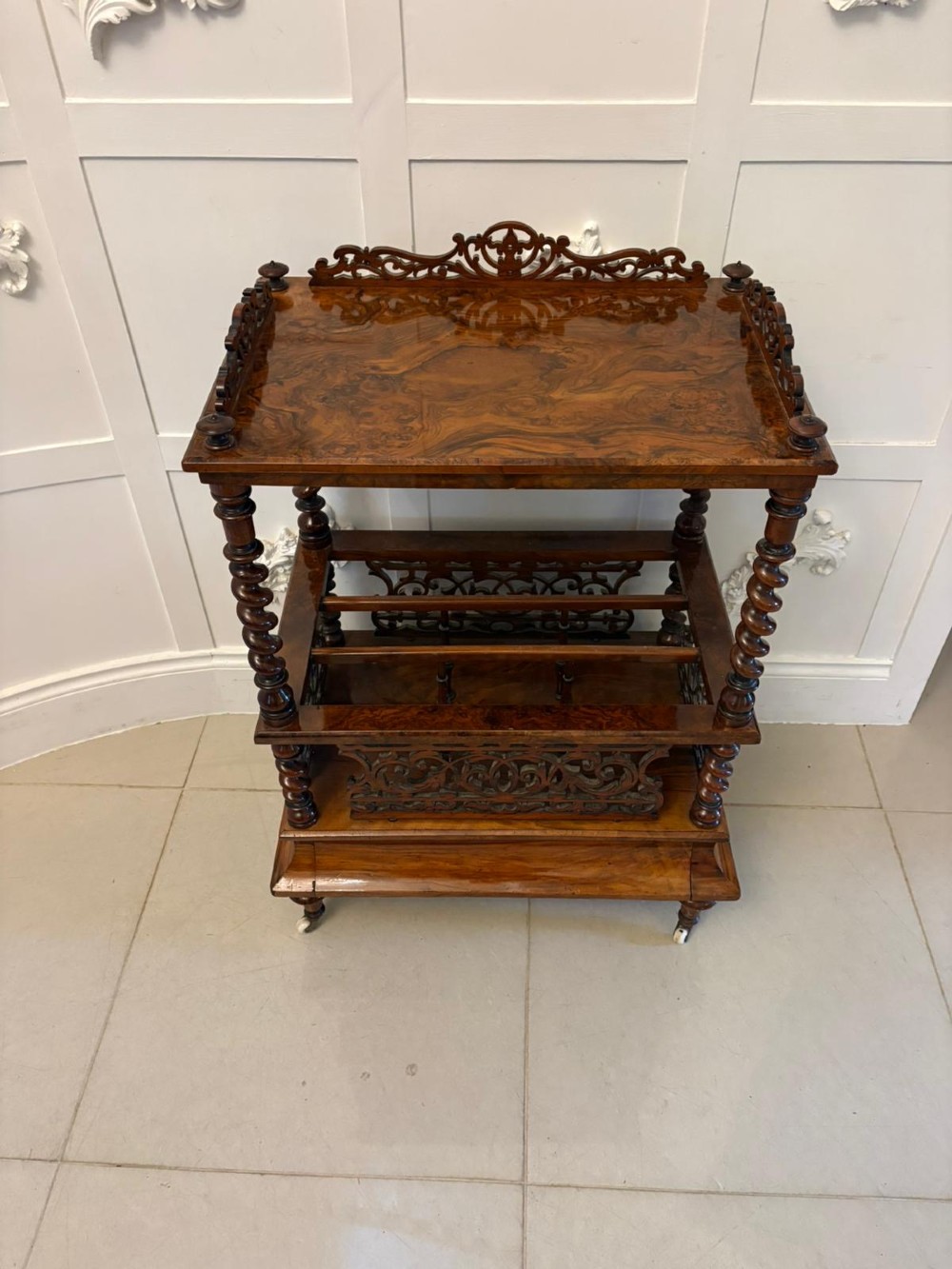 A Victorian burr walnut Canterbury featuring a top surface with a pierced fretwork gallery, barley twist supports, divided slots, and a single drawer resting on porcelain castors. View XI