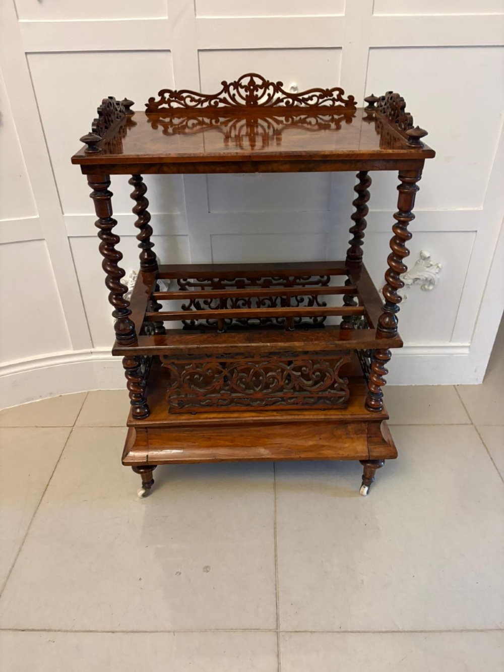A Victorian burr walnut Canterbury featuring a top surface with a pierced fretwork gallery, barley twist supports, divided slots, and a single drawer resting on porcelain castors. View XII
