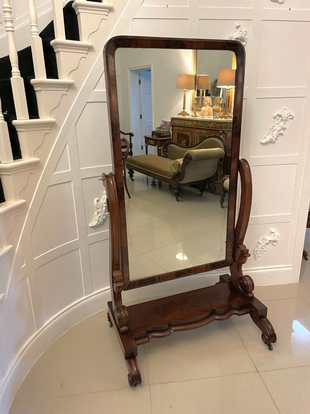 A full-length Victorian mahogany cheval mirror featuring a rounded rectangular swivelling frame, carved scroll uprights, a shaped plinth base, and brass castors.