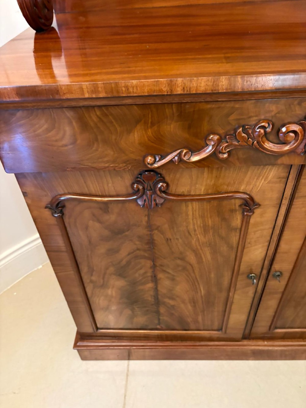 A Victorian mahogany chiffonier featuring a two-tiered upper shelf superstructure with carved scroll supports and a lower cupboard with flame mahogany veneered doors. View II