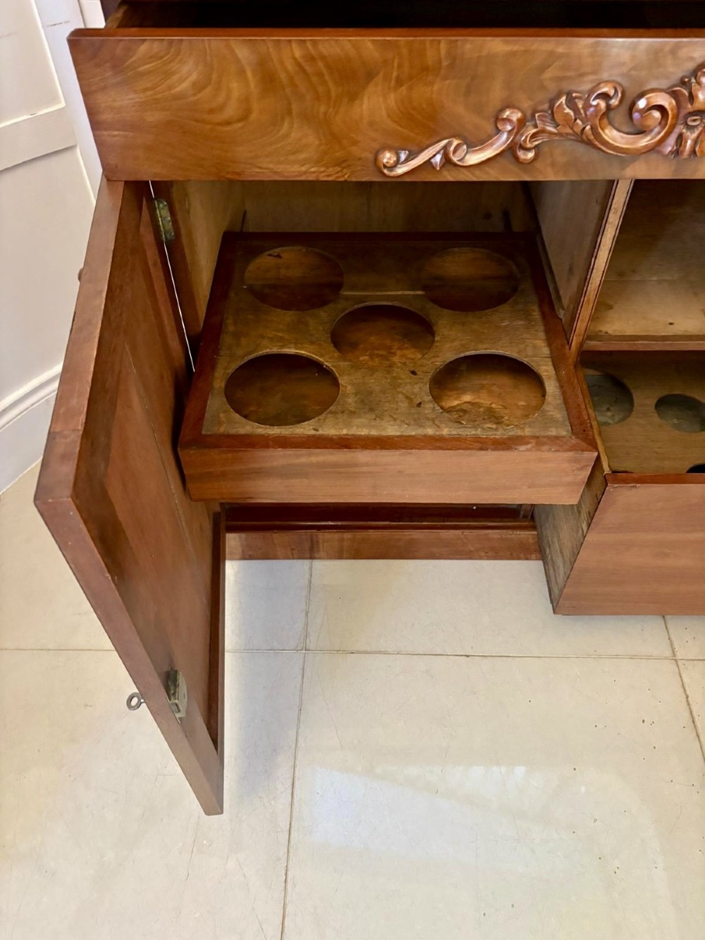 A Victorian mahogany chiffonier featuring a two-tiered upper shelf superstructure with carved scroll supports and a lower cupboard with flame mahogany veneered doors. View V