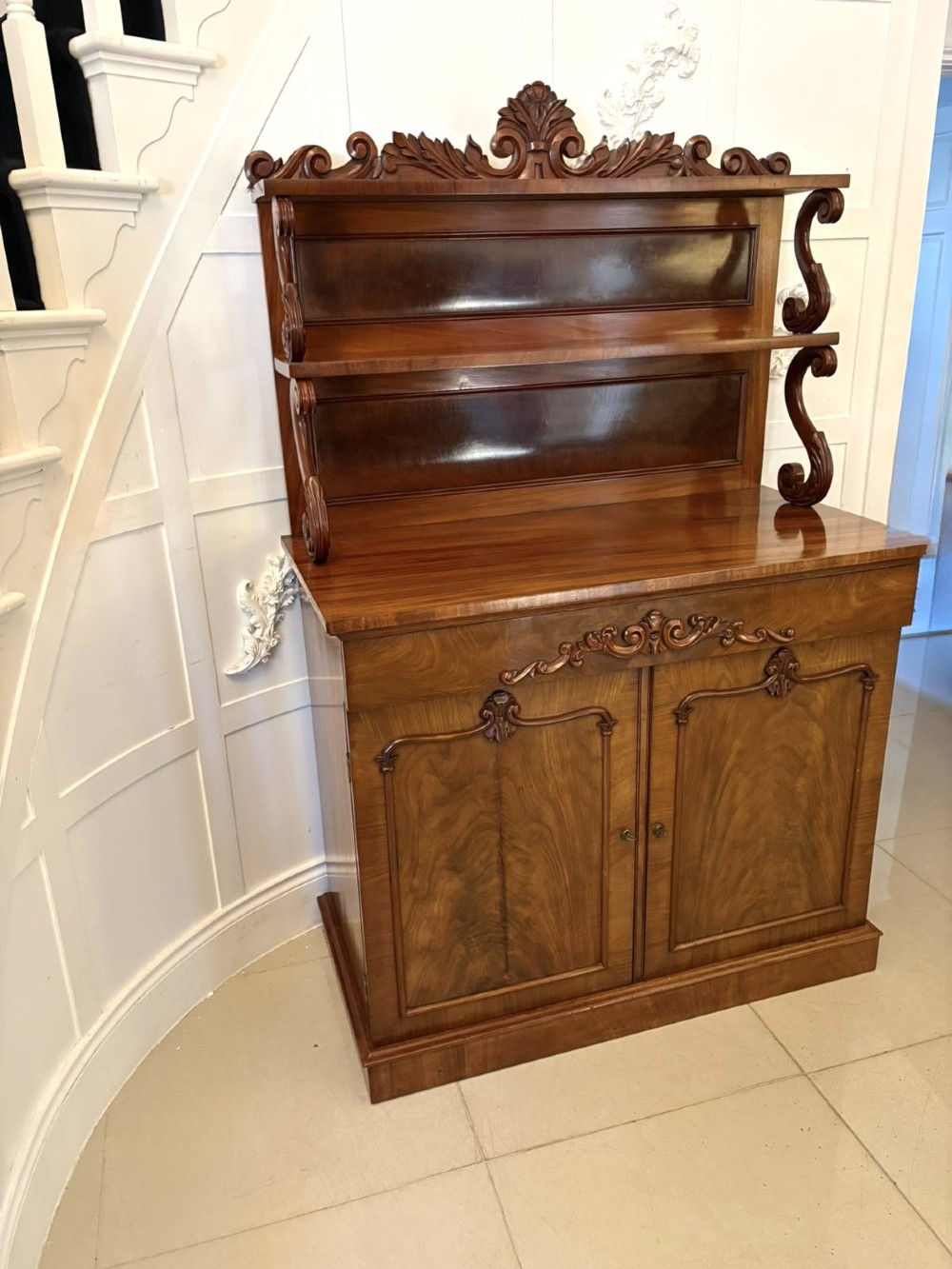 A Victorian mahogany chiffonier featuring a two-tiered upper shelf superstructure with carved scroll supports and a lower cupboard with flame mahogany veneered doors. View XII