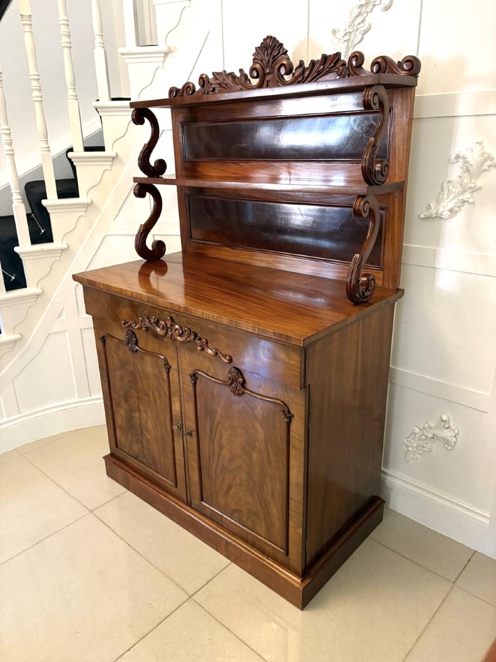 A Victorian mahogany chiffonier featuring a two-tiered upper shelf superstructure with carved scroll supports and a lower cupboard with flame mahogany veneered doors. View XIII