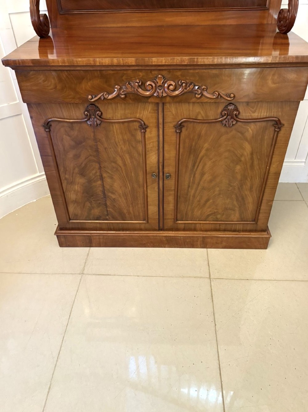 A Victorian mahogany chiffonier featuring a two-tiered upper shelf superstructure with carved scroll supports and a lower cupboard with flame mahogany veneered doors. View XIV