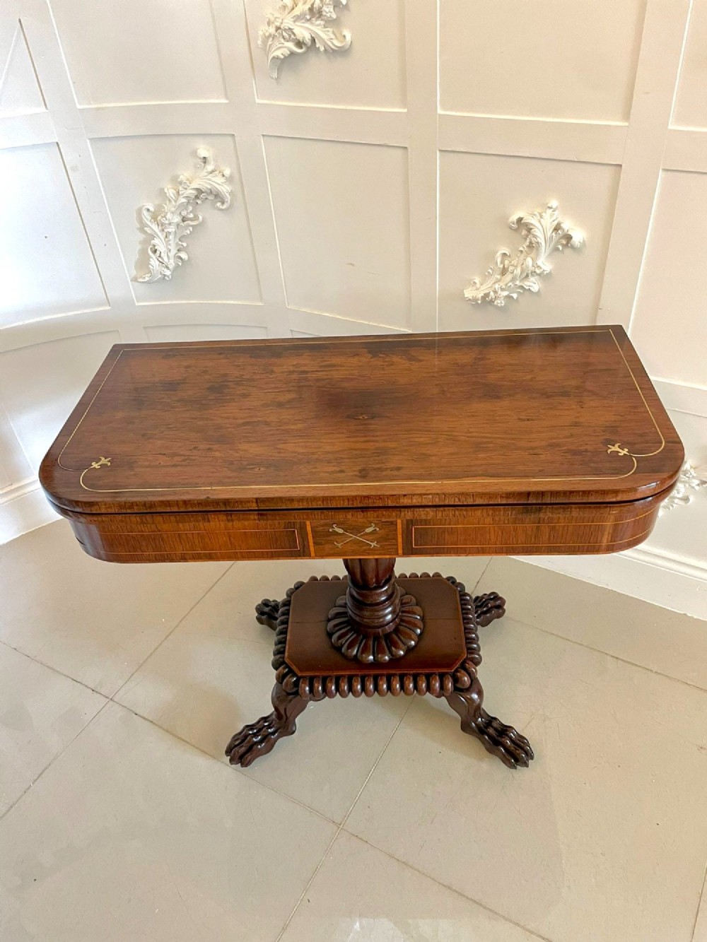 A Regency fold-over rosewood card table with brass inlay, a central pedestal, and carved lion paw feet. View V