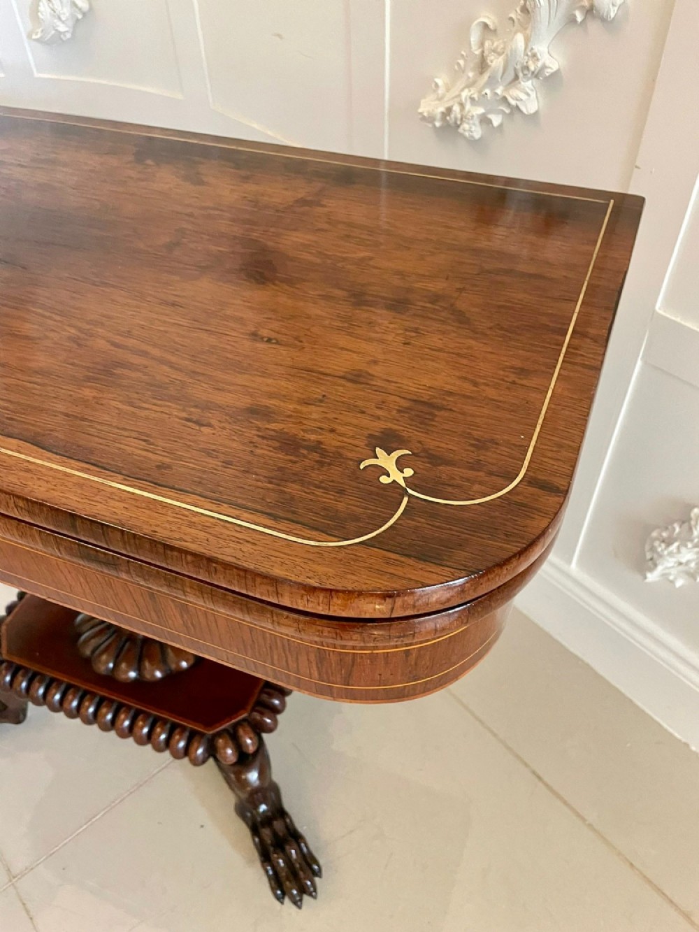 A Regency fold-over rosewood card table with brass inlay, a central pedestal, and carved lion paw feet. View X