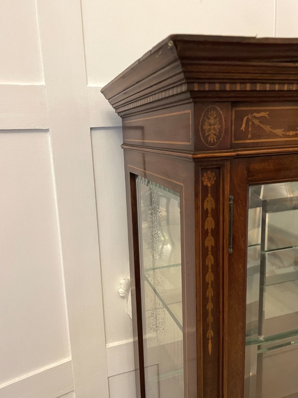 An antique mahogany display cabinet featuring a swan neck pediment, marquetry inlays, glazed double doors, interior glass shelves, and square tapered legs. View X