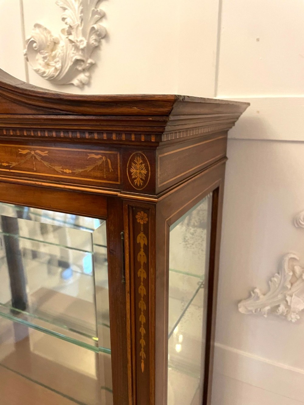An antique mahogany display cabinet featuring a swan neck pediment, marquetry inlays, glazed double doors, interior glass shelves, and square tapered legs. View XI