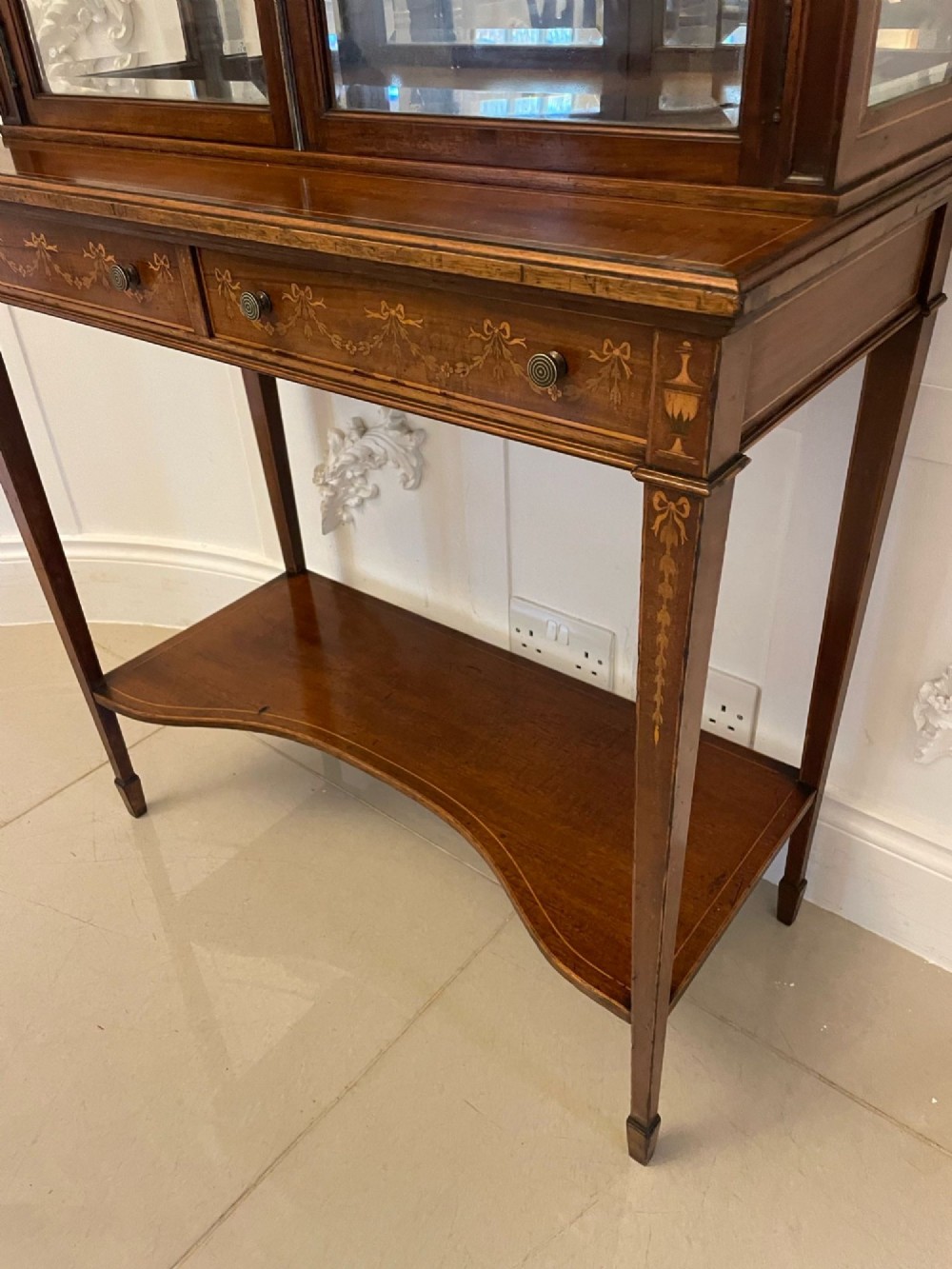 An antique mahogany display cabinet featuring a swan neck pediment, marquetry inlays, glazed double doors, interior glass shelves, and square tapered legs. View XIII