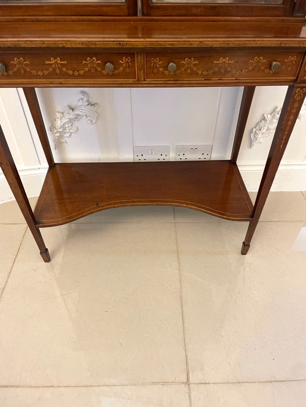 An antique mahogany display cabinet featuring a swan neck pediment, marquetry inlays, glazed double doors, interior glass shelves, and square tapered legs. View XIV