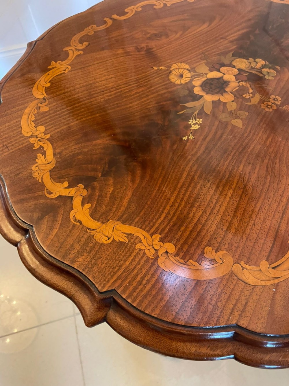 A Victorian walnut occasional table featuring a scalloped rim, intricate marquetry floral inlay on the tabletop, a turned central pedestal, and three carved cabriole legs. View II