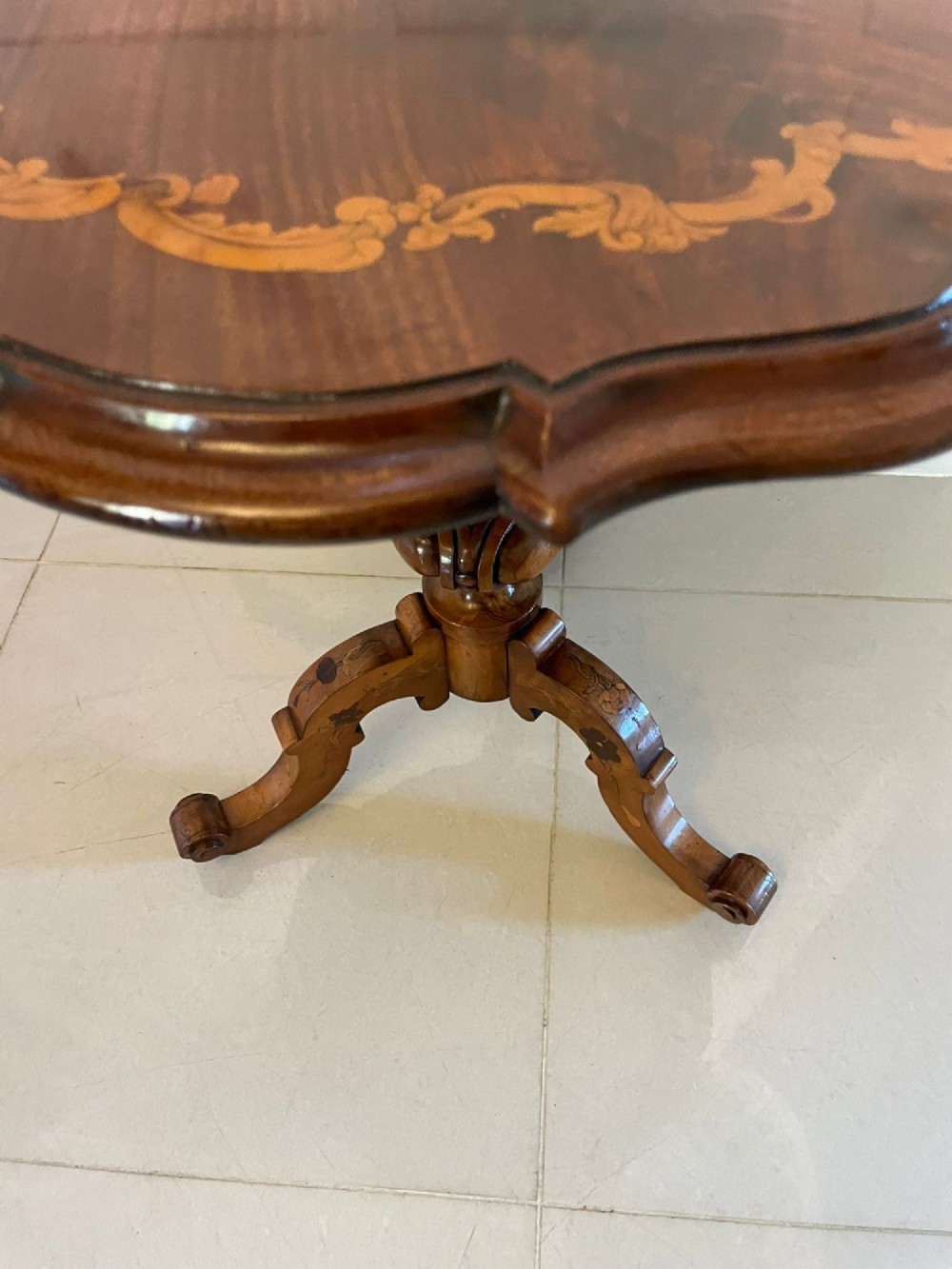 A Victorian walnut occasional table featuring a scalloped rim, intricate marquetry floral inlay on the tabletop, a turned central pedestal, and three carved cabriole legs. View III