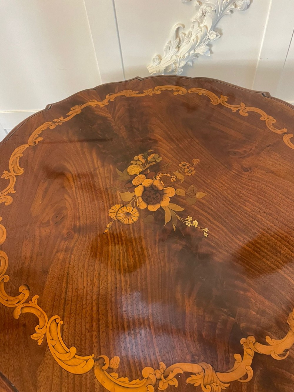 A Victorian walnut occasional table featuring a scalloped rim, intricate marquetry floral inlay on the tabletop, a turned central pedestal, and three carved cabriole legs. View V