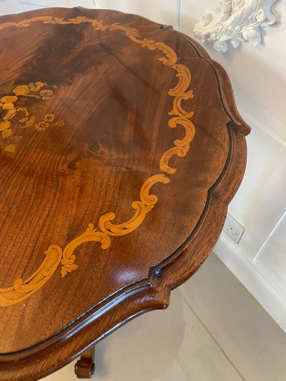 A Victorian walnut occasional table featuring a scalloped rim, intricate marquetry floral inlay on the tabletop, a turned central pedestal, and three carved cabriole legs. View VI