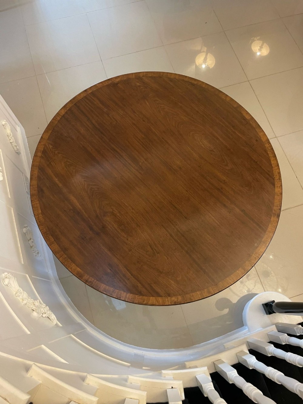 A circular George III figured mahogany tilt-top dining table positioned vertically on a four-legged pedestal base with brass castors. View II