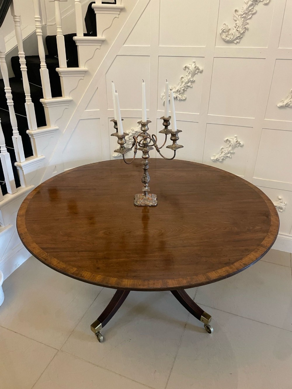 A circular George III figured mahogany tilt-top dining table positioned vertically on a four-legged pedestal base with brass castors. View V