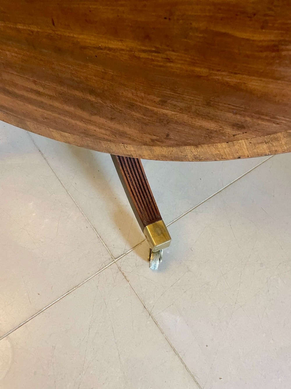 A circular George III figured mahogany tilt-top dining table positioned vertically on a four-legged pedestal base with brass castors. View VI