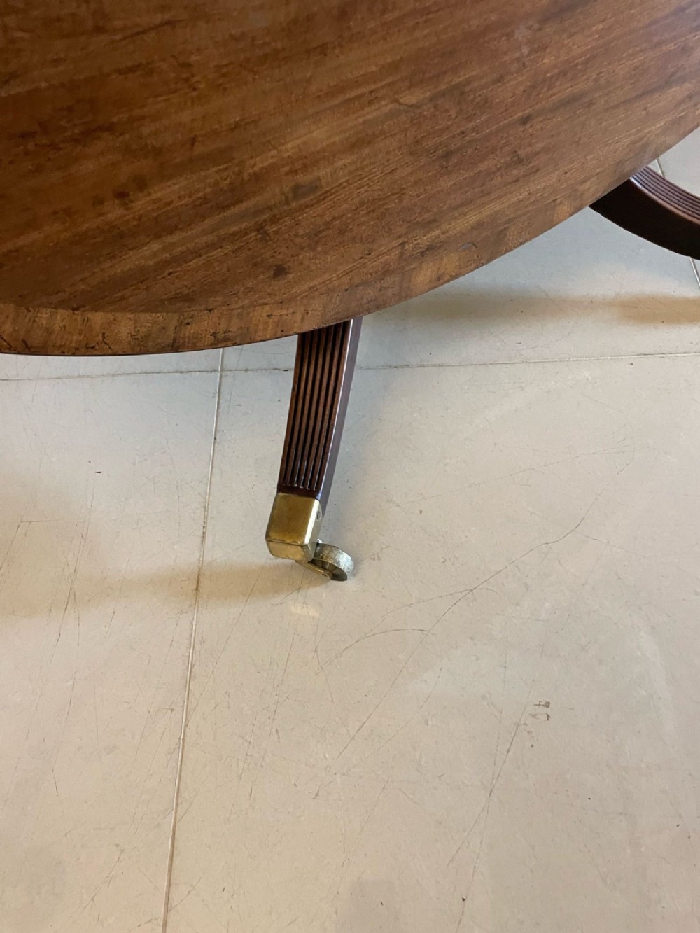 A circular George III figured mahogany tilt-top dining table positioned vertically on a four-legged pedestal base with brass castors. View VIII