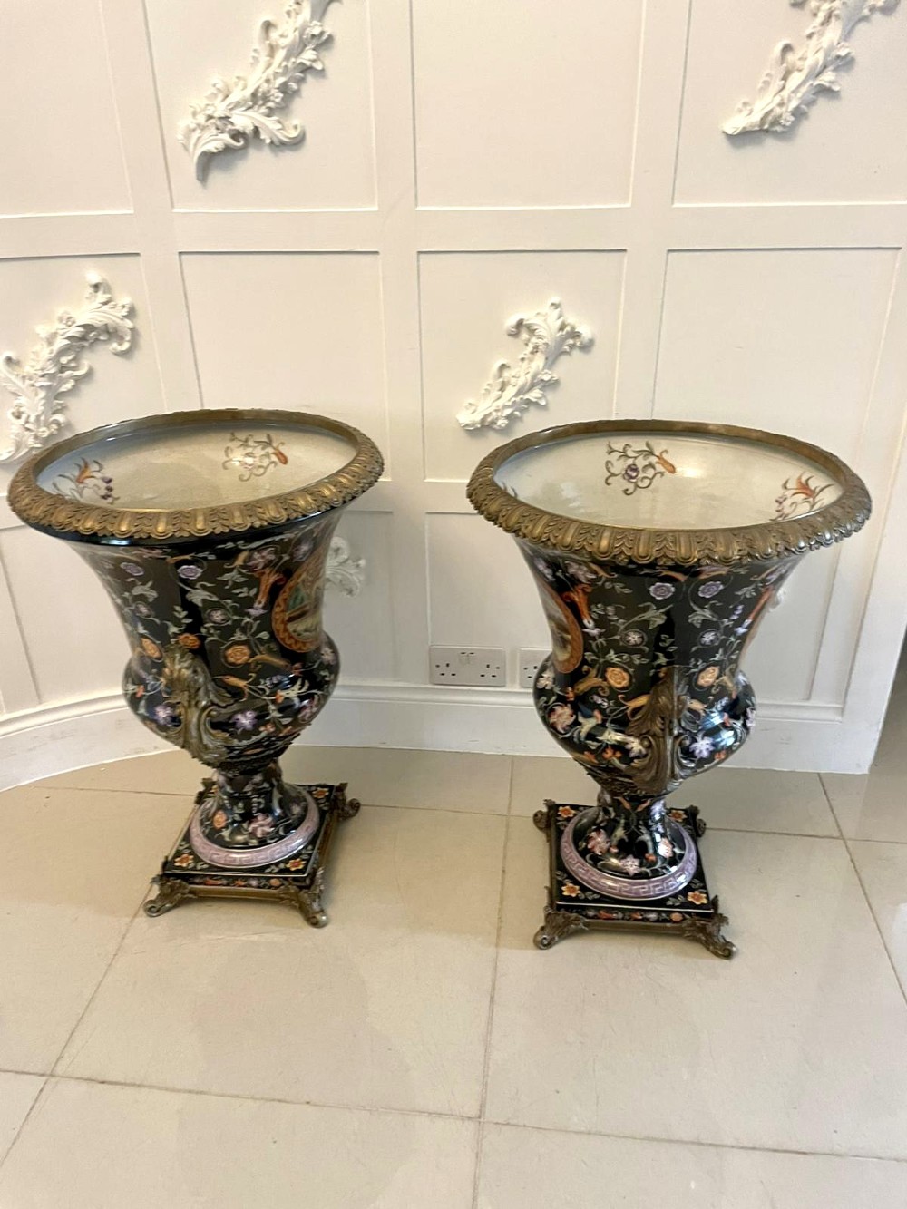 A pair of black French porcelain jardiniere urns featuring polychrome floral enamel, central painted animal reserves, and gadrooned brass mounts on square plinths. View VIII