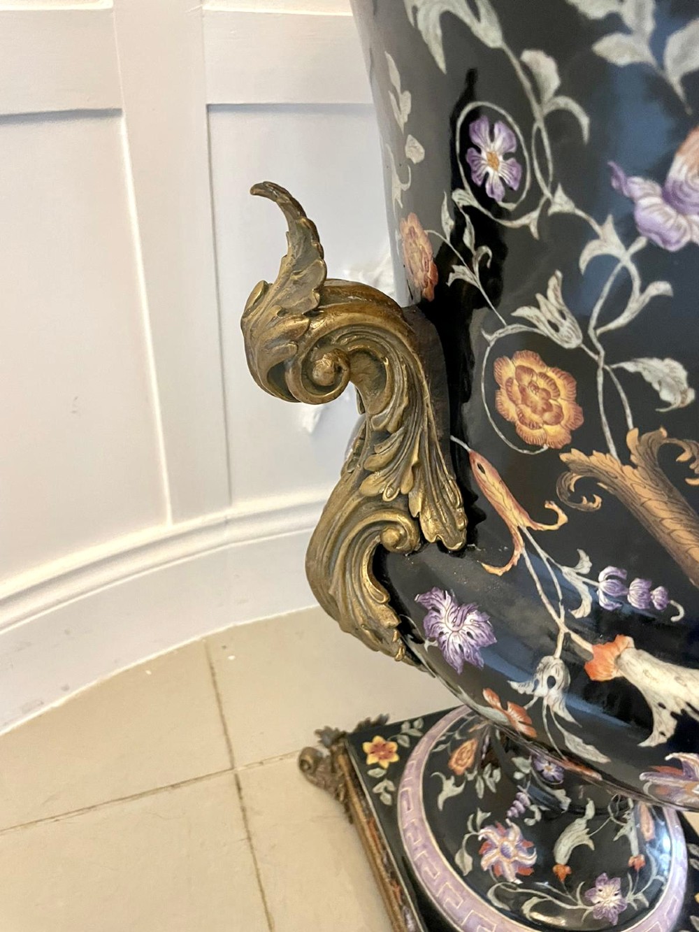 A pair of black French porcelain jardiniere urns featuring polychrome floral enamel, central painted animal reserves, and gadrooned brass mounts on square plinths. View IX