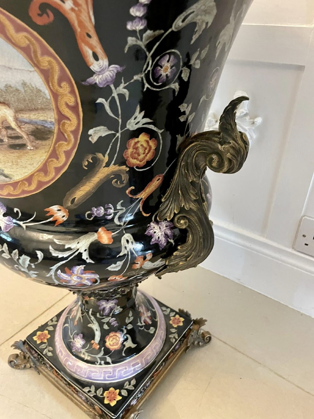 A pair of black French porcelain jardiniere urns featuring polychrome floral enamel, central painted animal reserves, and gadrooned brass mounts on square plinths. View XI