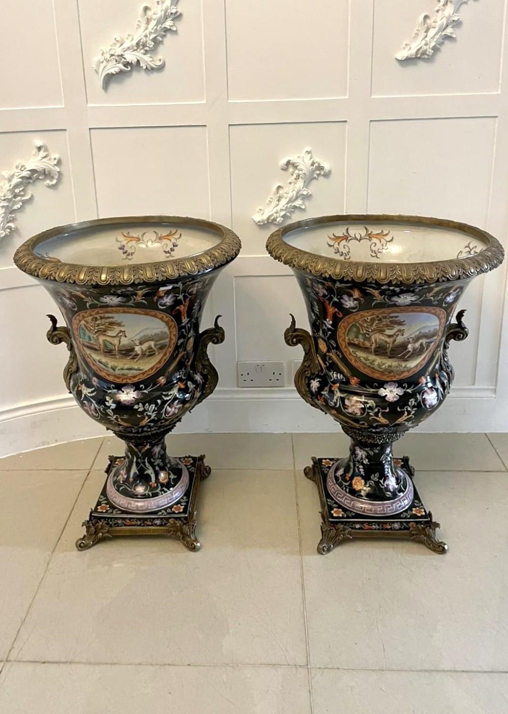 A pair of black French porcelain jardiniere urns featuring polychrome floral enamel, central painted animal reserves, and gadrooned brass mounts on square plinths. View XIII