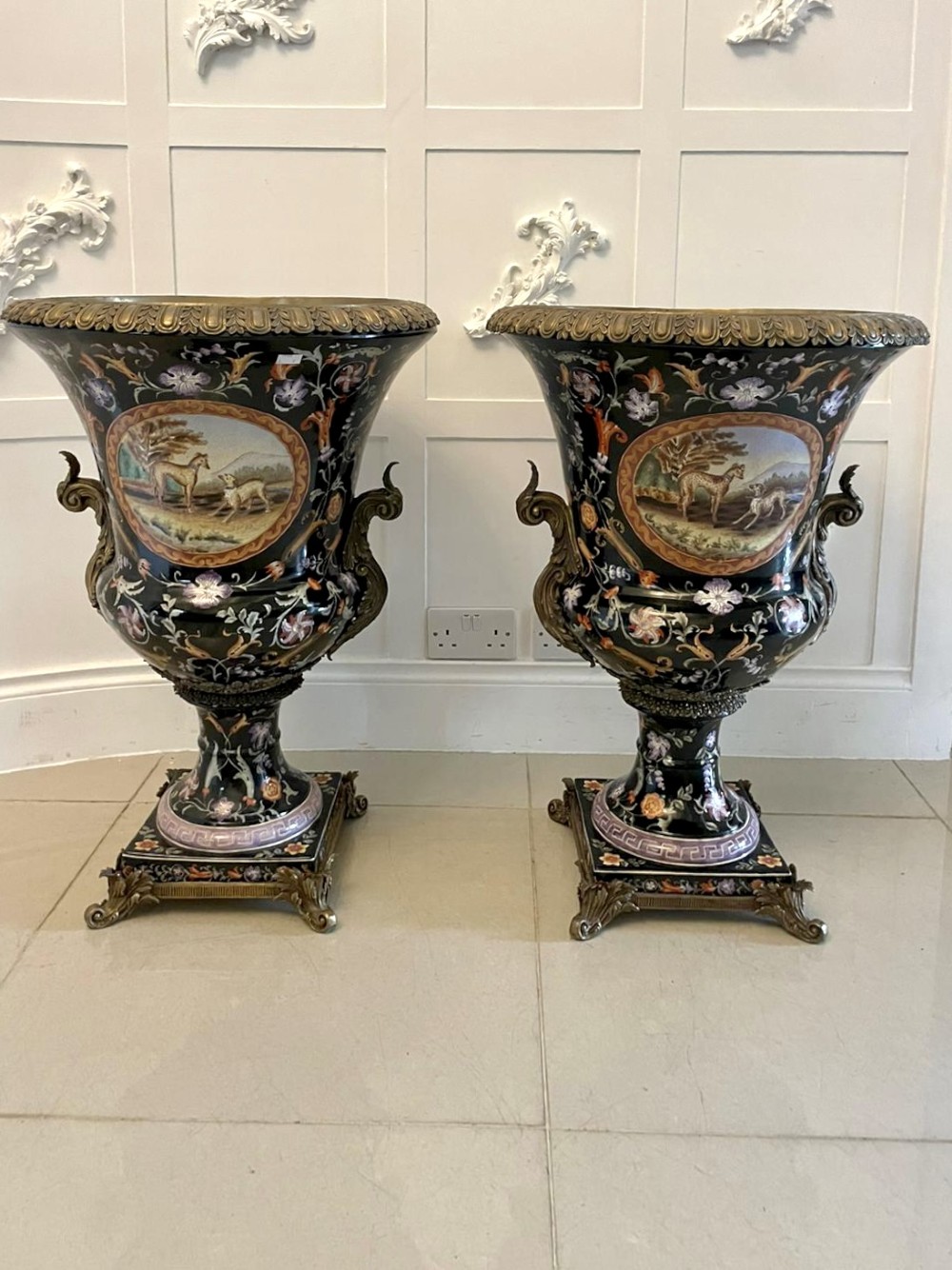 A pair of black French porcelain jardiniere urns featuring polychrome floral enamel, central painted animal reserves, and gadrooned brass mounts on square plinths. View XIV