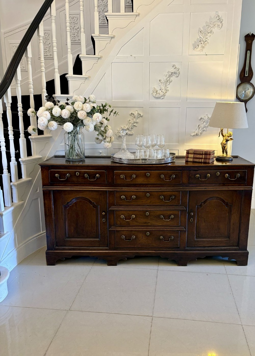 A George III dark oak dresser base featuring multiple drawers, arched cupboard doors, and brass swan-neck handles. View V