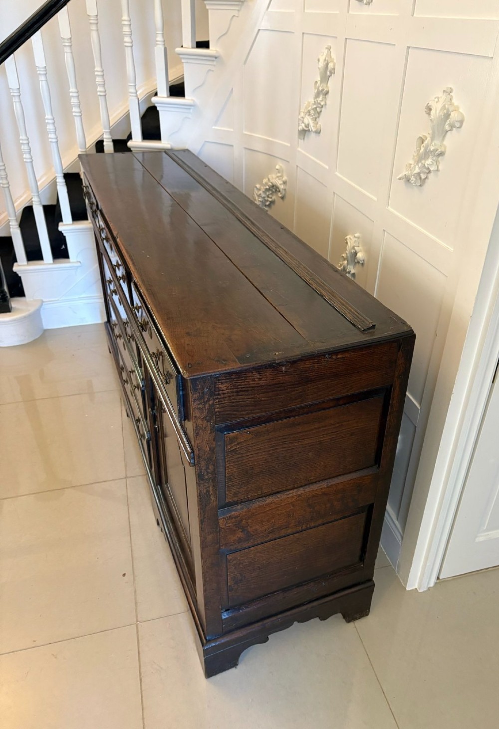 A George III dark oak dresser base featuring multiple drawers, arched cupboard doors, and brass swan-neck handles. View VI