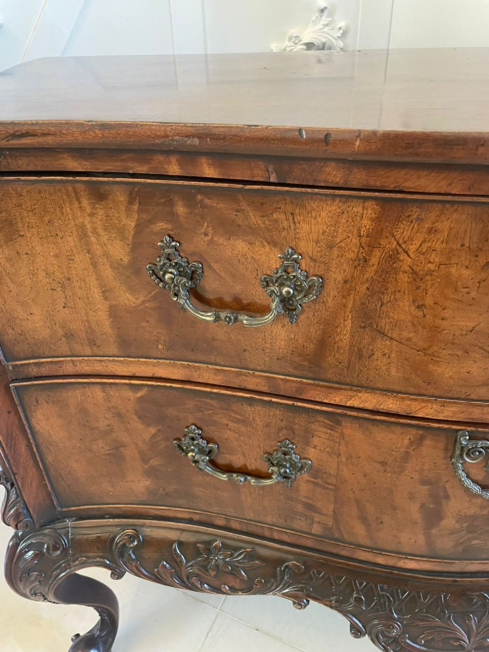 A Victorian figured mahogany serpentine chest of drawers featuring two drawers with cast brass handles, a deeply carved apron, and cabriole legs. View III