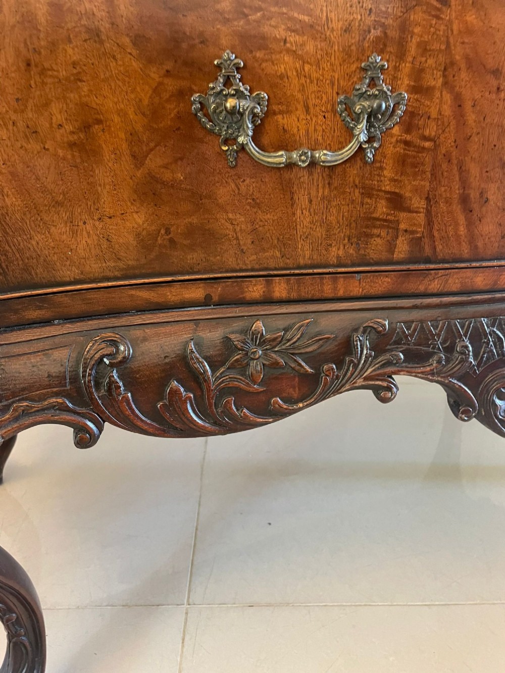 A Victorian figured mahogany serpentine chest of drawers featuring two drawers with cast brass handles, a deeply carved apron, and cabriole legs. View IV