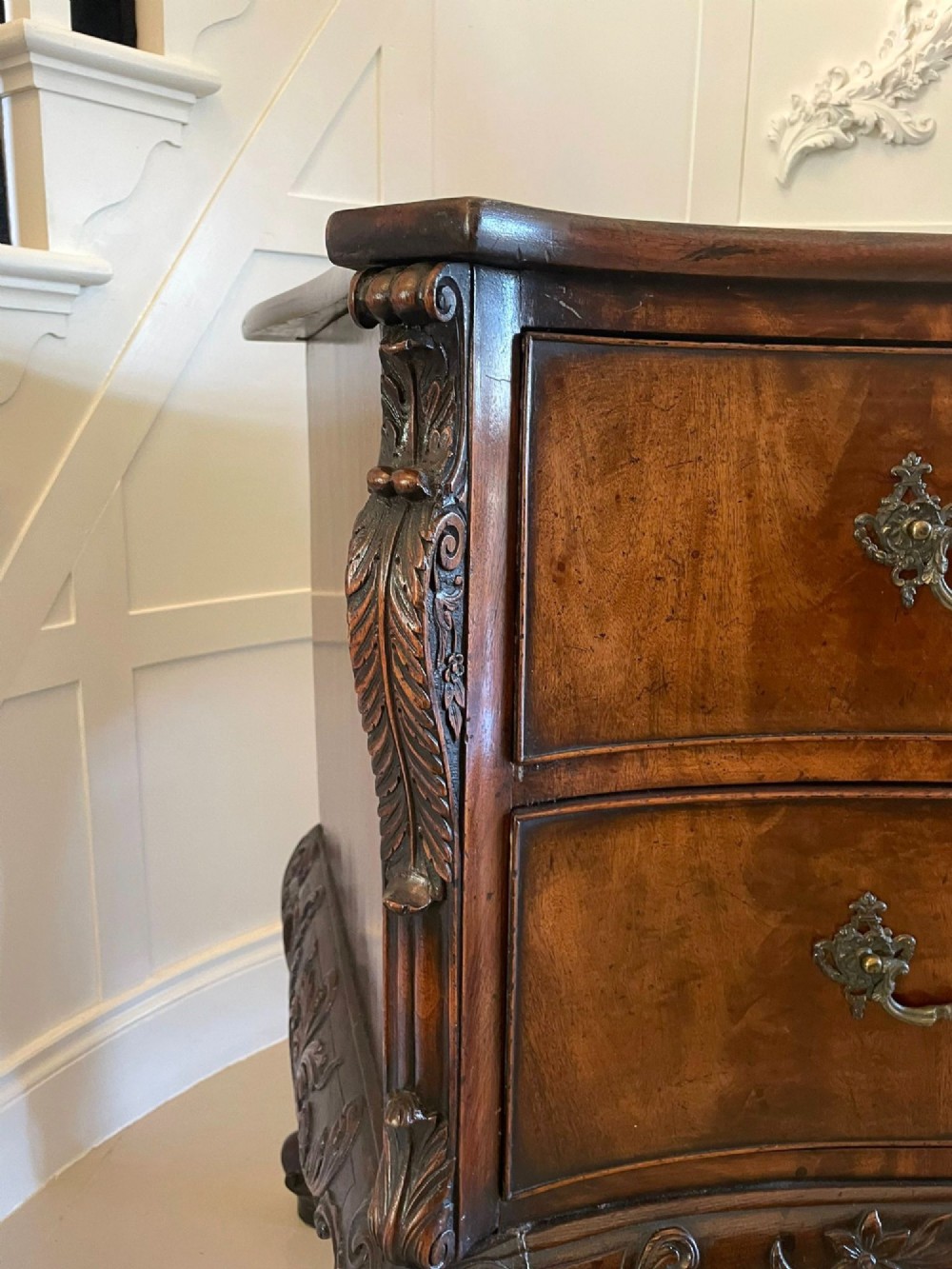 A Victorian figured mahogany serpentine chest of drawers featuring two drawers with cast brass handles, a deeply carved apron, and cabriole legs. View VIII