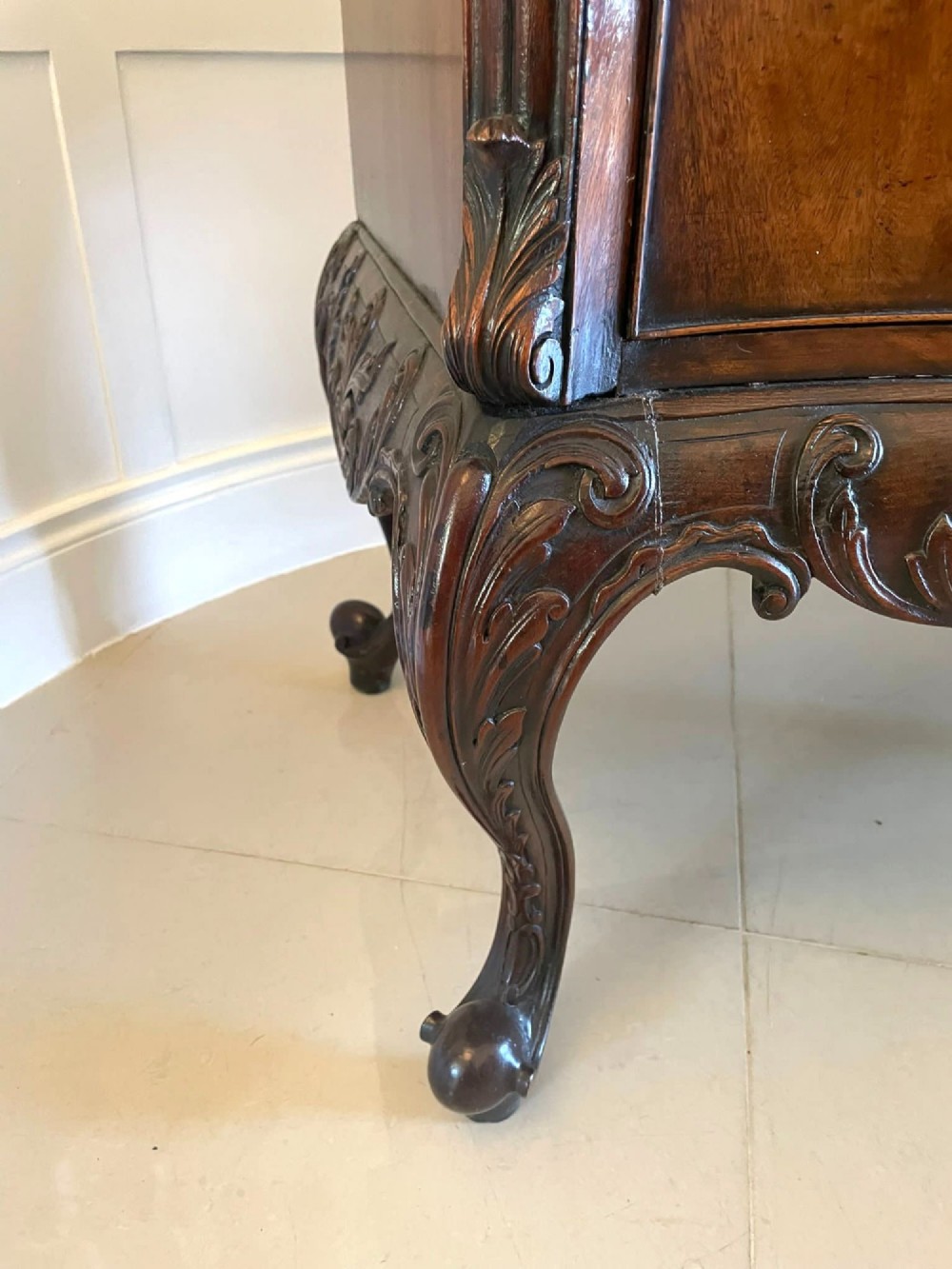 A Victorian figured mahogany serpentine chest of drawers featuring two drawers with cast brass handles, a deeply carved apron, and cabriole legs. View X