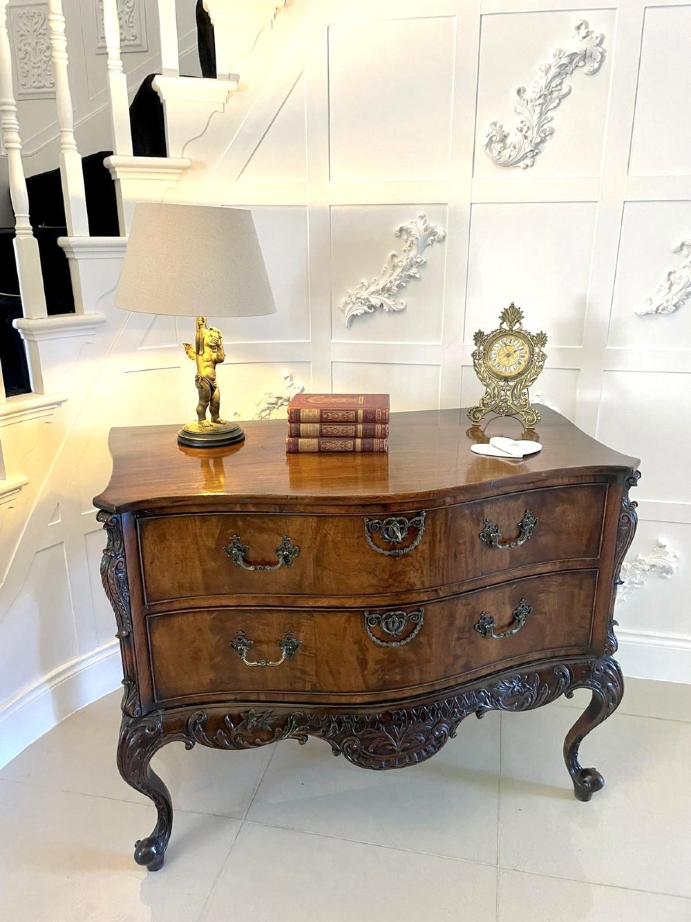 A Victorian figured mahogany serpentine chest of drawers featuring two drawers with cast brass handles, a deeply carved apron, and cabriole legs. View XII