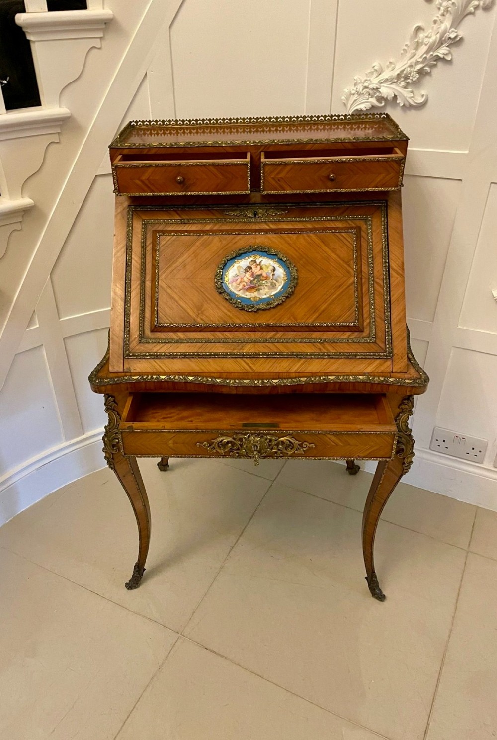 A French Rococo revival slant-front kingwood bureau featuring delicate ormolu mounts, a central hand-painted porcelain plaque, and elegant cabriole legs. View XII