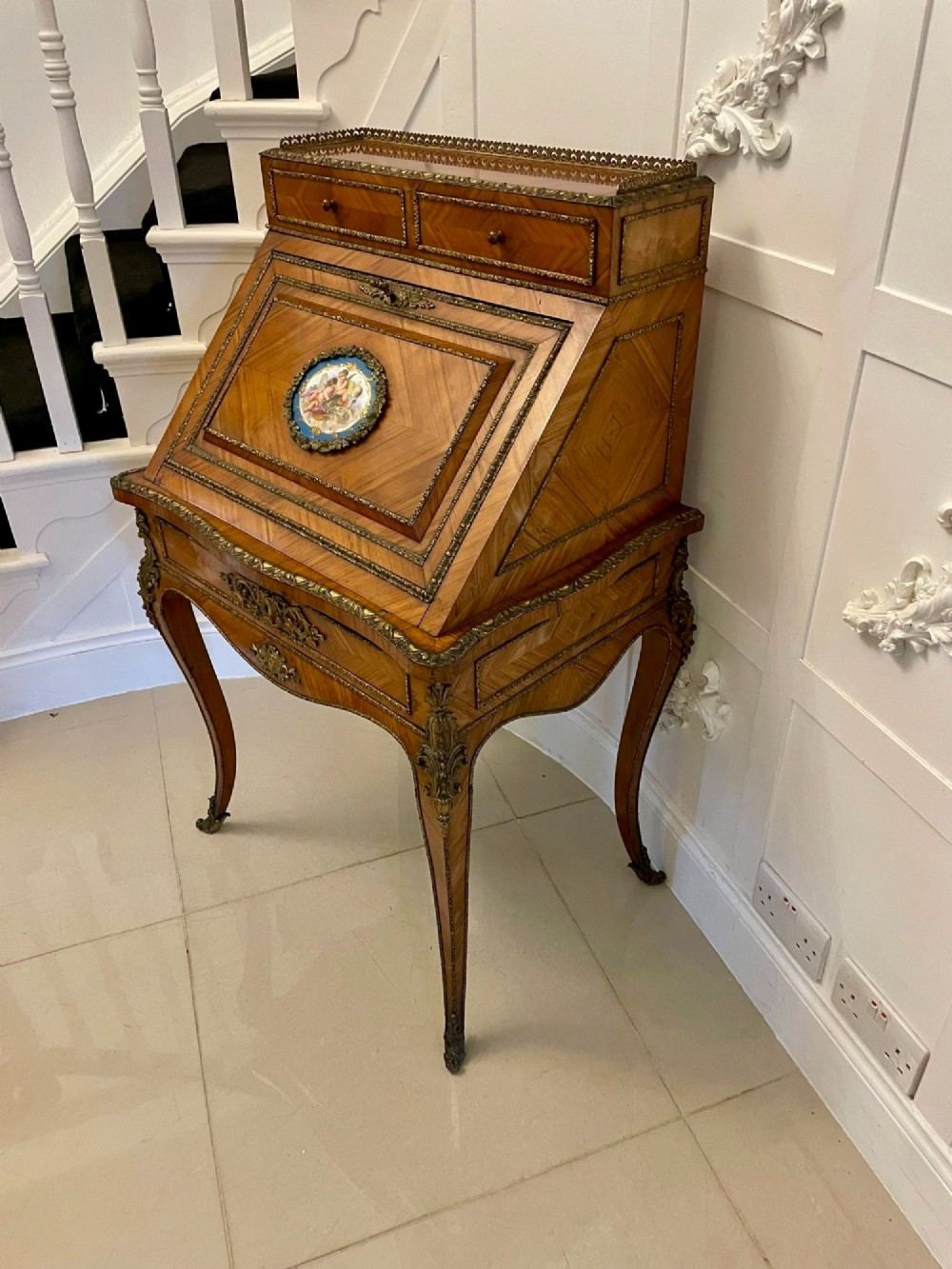 A French Rococo revival slant-front kingwood bureau featuring delicate ormolu mounts, a central hand-painted porcelain plaque, and elegant cabriole legs. View XIV