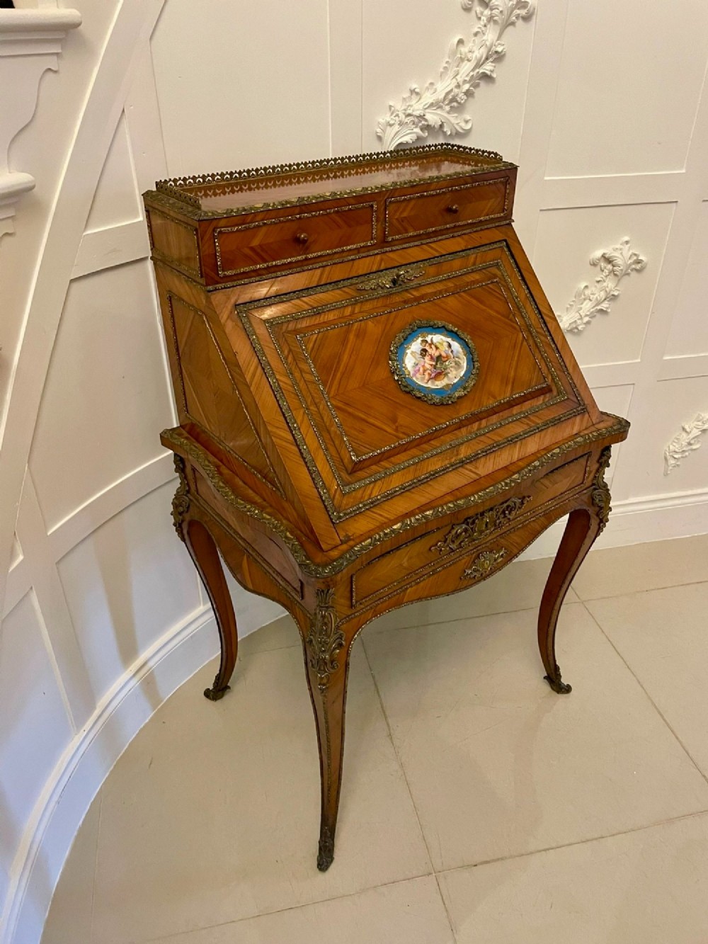 A French Rococo revival slant-front kingwood bureau featuring delicate ormolu mounts, a central hand-painted porcelain plaque, and elegant cabriole legs.